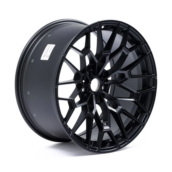 A glossy black alloy wheel with a complex, multi-spoke design is standing upright, highlighting its intricate geometric pattern against a plain white background. A label with text is visible on the rim’s inner surface.