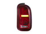 A red car taillight features a distinctive Union Jack pattern and an illuminated orange strip, set against a plain white background.