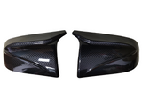 Two glossy carbon fiber car mirror covers, resting side by side against a white background, highlighting their sleek, aerodynamic design and polished finish.