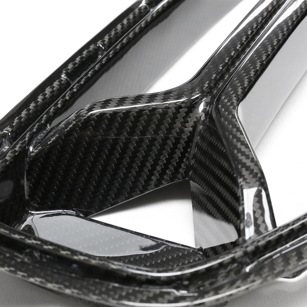 Carbon fiber panel with a glossy finish, featuring intricate weaving patterns, lies on a flat surface. It appears structured and rigid, likely part of an automotive or industrial component.