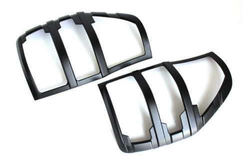 Black plastic tail light covers are lying side by side on a plain white background. They have curved, segmented designs to fit over vehicle tail lights, providing a protective and decorative function.
