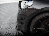 A black car's front corner, including the headlight and tire, is shown on a checkered-patterned floor, emphasizing its sleek design and glossy finish.