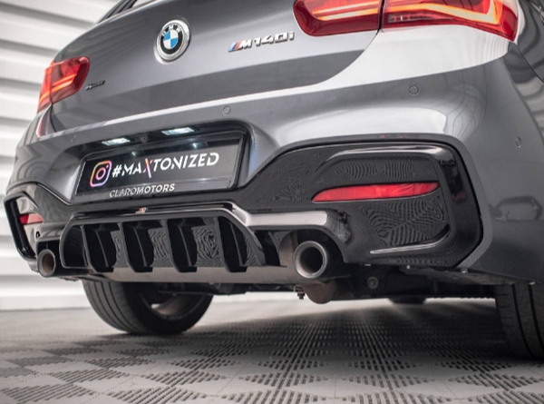 A gray BMW M140i rear view features dual exhaust pipes, sporty diffuser, and red taillights. It sits on textured flooring within a bright, enclosed space. The license plate reads "#MAXTONIZED CIARMOTORS."