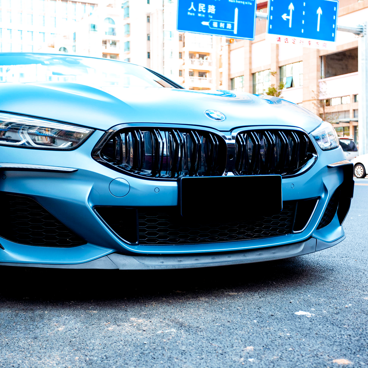 A blue car with a sleek design is parked on a city street. Overhead, road signs feature arrows and Chinese characters, surrounded by buildings and other vehicles.
