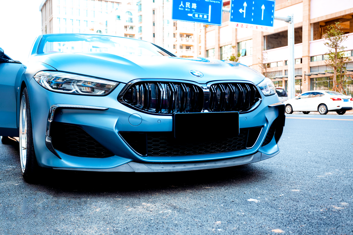 A blue car with a sleek design is parked on a city street. Overhead, road signs feature arrows and Chinese characters, surrounded by buildings and other vehicles.