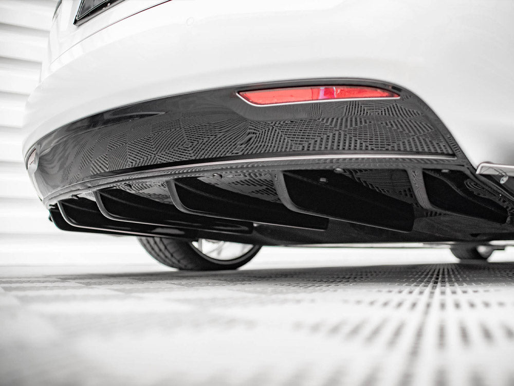 The lower rear section of a white car displays a patterned black diffuser, situated in a well-lit, indoor space with a checkered floor.