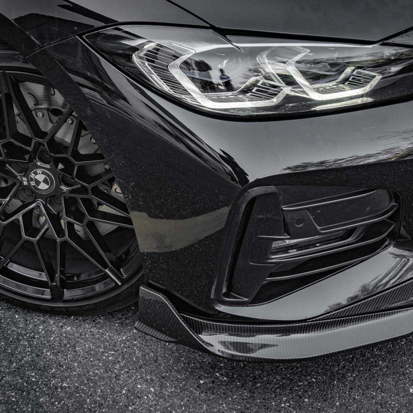 Black car with intricate alloy wheel design and sleek headlight, parked on an asphalt surface. Reflections highlight the car's glossy finish. BMW badge visible on the wheel hub.