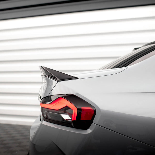 A sleek car's rear with an illuminated taillight and prominent spoiler, parked in front of a white, horizontal-panel garage door.