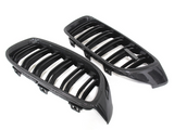 Two carbon fiber car grilles with slatted designs lying side by side on a plain white background. The grilles have shiny, textured surfaces and a sleek, aerodynamic shape.