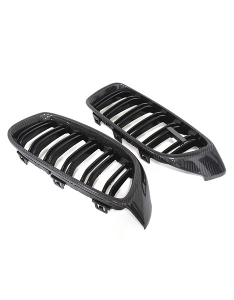 Two carbon fiber car grilles with slatted designs lying side by side on a plain white background. The grilles have shiny, textured surfaces and a sleek, aerodynamic shape.