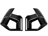 Two angular carbon fiber car parts face each other, featuring sleek lines and sharp edges, set against a plain white background.
