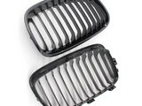 Two black, oval-shaped car grilles with vertical slats are positioned on a white background, suggesting automotive components ready for installation or inspection.