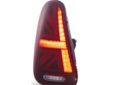 A triangular taillight displays a bright red and amber pattern reminiscent of the Union Jack. It is illuminated against a plain white background, highlighting its design.
