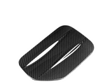 A rectangular, carbon fiber vent cover with two slits is angled diagonally against a plain white background.