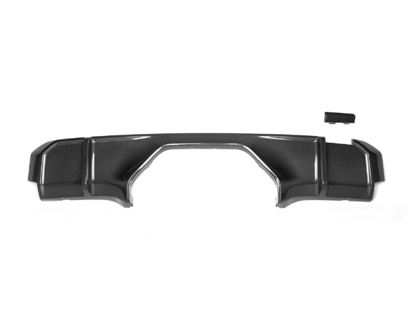 A carbon fiber car bumper diffuser lies flat against a white background, featuring a sleek, aerodynamic design with angular edges. A small rectangular piece is positioned above it.