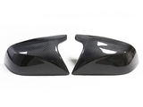 Two carbon fiber car mirror covers rest side by side on a white background, showcasing their glossy, patterned surface and aerodynamic design.
