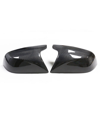 Two carbon fiber car mirror covers rest side by side on a white background, showcasing their glossy, patterned surface and aerodynamic design.