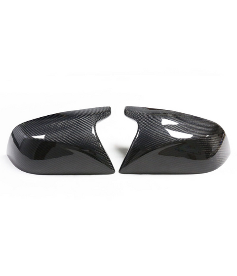 Two carbon fiber car mirror covers rest side by side on a white background, showcasing their glossy, patterned surface and aerodynamic design.