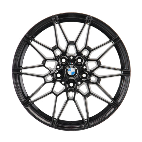 A black, intricately designed alloy wheel rim with the BMW logo at its center, viewed directly from the front, set against a plain white background.