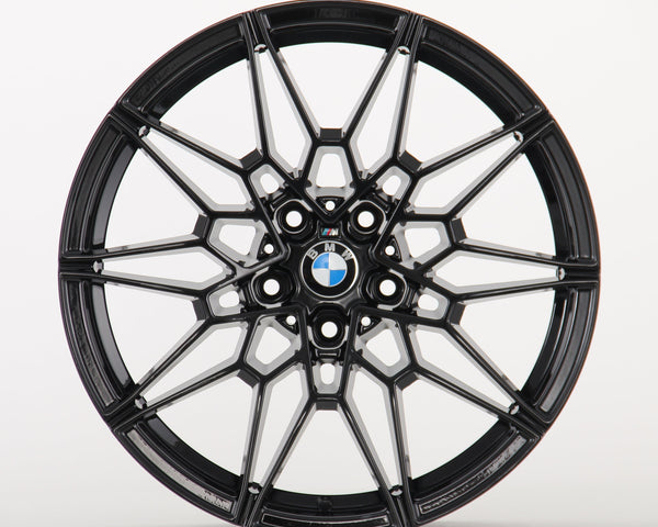 A black, multi-spoke alloy wheel displays a BMW logo at the center, set against a plain white background, highlighting its intricate design.