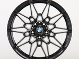 Black, intricately designed alloy wheel with a BMW logo in the center; it rests against a plain white background.
