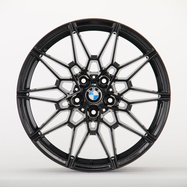 Black, intricately designed alloy wheel with a BMW logo in the center; it rests against a plain white background.