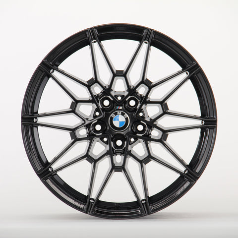 A black, intricately designed car wheel rim with a central BMW logo is displayed against a plain white background, showcasing its geometric pattern and sleek finish.