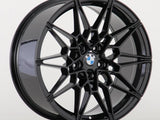 A black, multi-spoke car wheel rim features a central BMW logo, set against a plain white background.