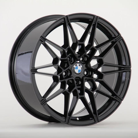 A black, multi-spoke car wheel rim features a central BMW logo, set against a plain white background.