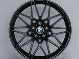A sleek black alloy wheel with a multi-spoke design, featuring the BMW logo at its center, stands on a plain circular platform in a light gray setting.