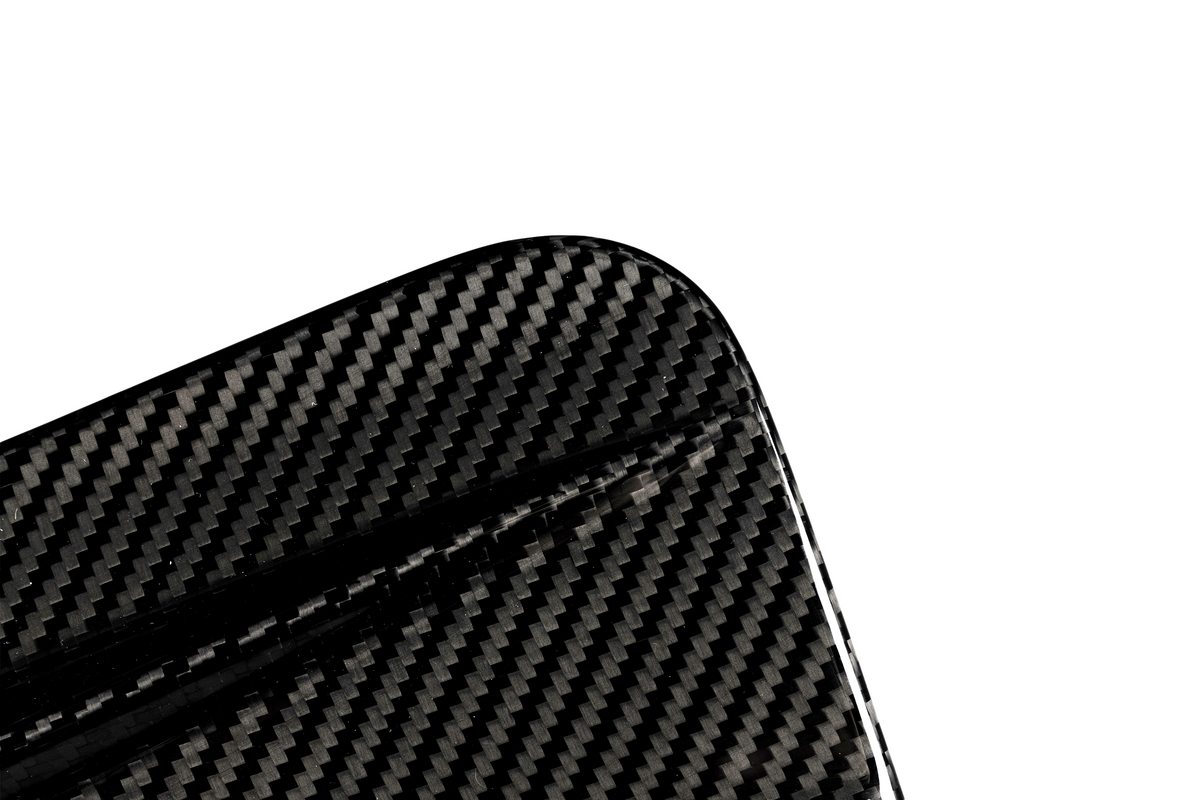 A close-up of a carbon fiber object with a visible textured pattern, featuring a rounded corner, set against a plain white background.