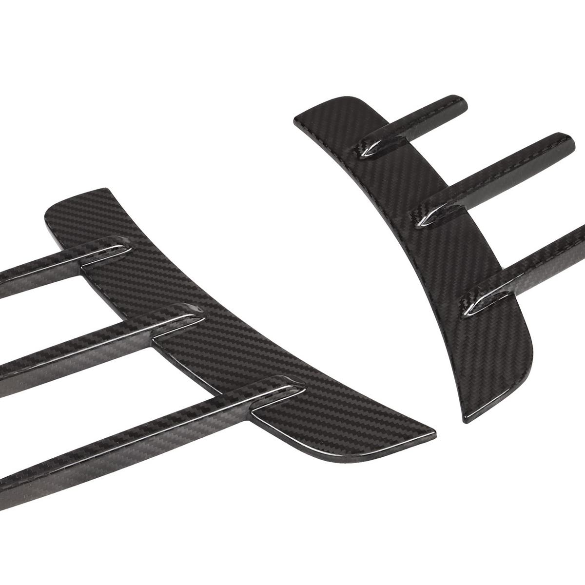 Carbon fiber car parts lie side by side, showcasing aerodynamic fin designs on a white background, highlighting their sleek and modern appearance.