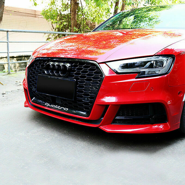 A red car with a prominent honeycomb grille displaying the word "quattro" is parked. The scene features greenery in the background under natural daylight.