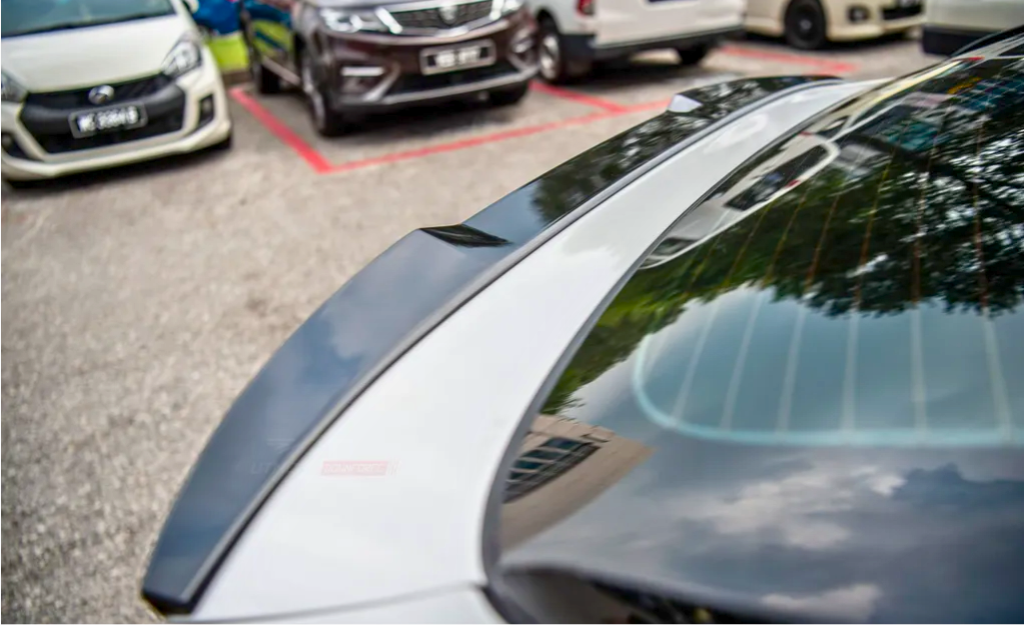 A car with a reflective rear windshield shows tree and building reflections, parked in a lot among other vehicles, delineated by red lines.