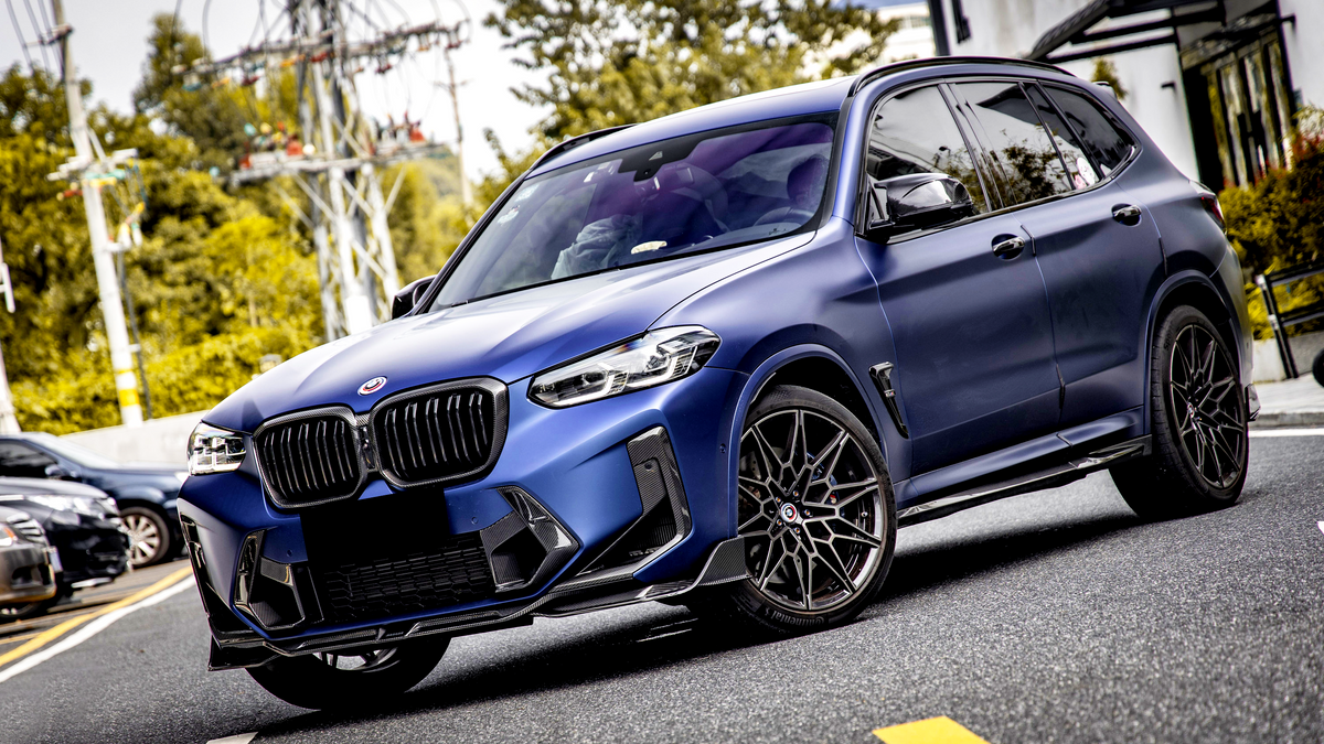 An SUV with a matte blue finish is parked on a street, featuring black grille and wheels, surrounded by trees and parked cars.