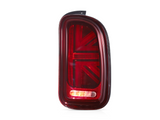 A red car taillight features a stylized Union Jack design. It is illuminated against a plain white background, showcasing its detailed pattern and glossy surface.