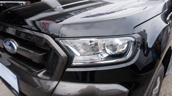 The image shows the front of a black Ford vehicle with a prominent headlight and the word "RANGER" embossed above the grille. It is parked outdoors on a concrete surface.