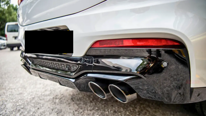 A white car's rear end is shown with dual exhaust pipes and a red taillight, parked on a gravel surface with another vehicle in the background.