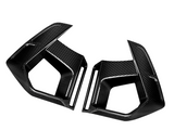 Two angular, carbon fiber car air vents, placed opposite each other, against a plain white background; their sleek, textured surfaces highlighting a modern, aerodynamic design.