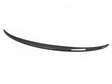 A long, black carbon fiber car spoiler sits against a plain white background, showcasing a sleek design and subtle curvature.