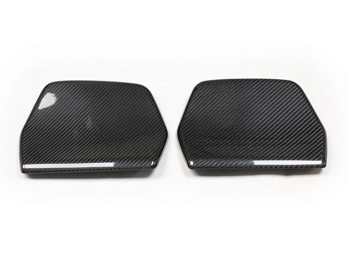 Two carbon fiber car mirror covers lie side by side on a plain white background, displaying a glossy texture and weave pattern, emphasizing their sleek, aerodynamic design.