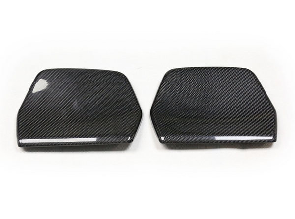 Two carbon fiber car mirror covers lie side by side on a plain white background, displaying a glossy texture and weave pattern, emphasizing their sleek, aerodynamic design.