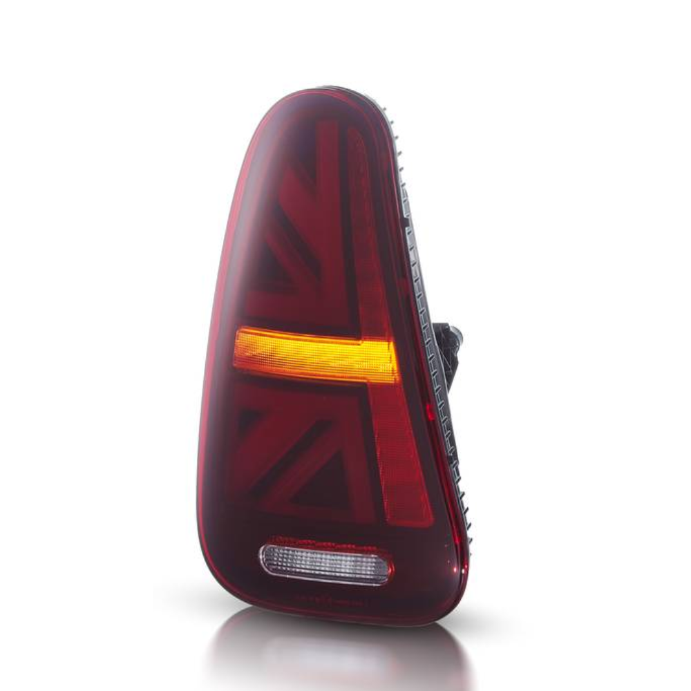 A sleek, triangular car taillight with a Union Jack design glows red and amber. It's positioned upright on a white reflective surface.