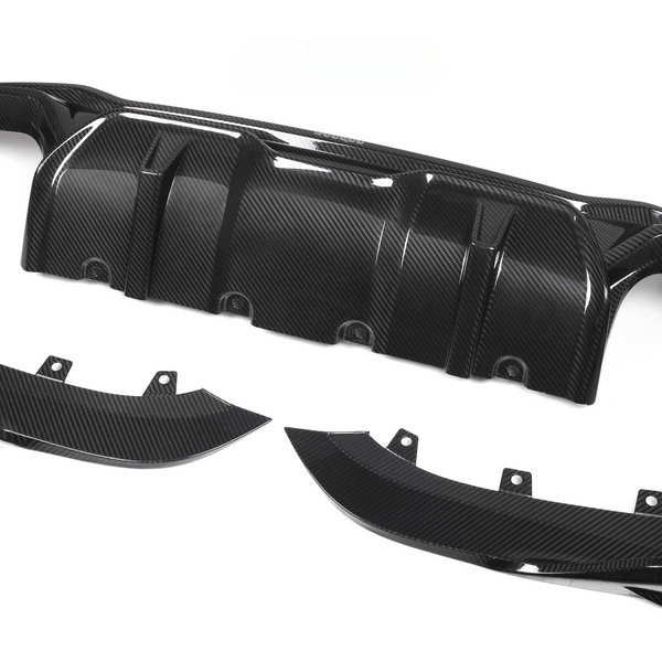 Carbon fiber car diffuser components lie on a white background. The main piece, with multiple ridges, is accompanied by two curved side parts, each featuring mounting brackets.