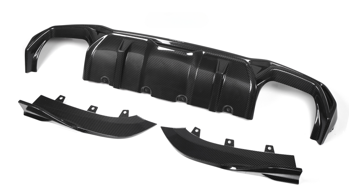 Carbon fiber car diffuser components lie on a white background. The main piece, with multiple ridges, is accompanied by two curved side parts, each featuring mounting brackets.