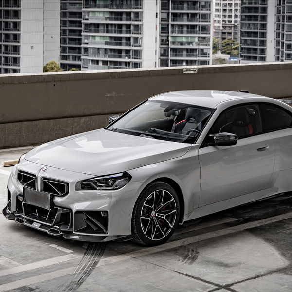 A sleek, silver sports car is parked on a rooftop, surrounded by tall urban buildings, under overcast skies.