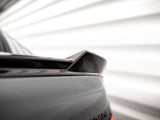 A car rear spoiler is positioned diagonally, set in a blurred, bright background with horizontal lines, suggesting a dynamic, modern environment.