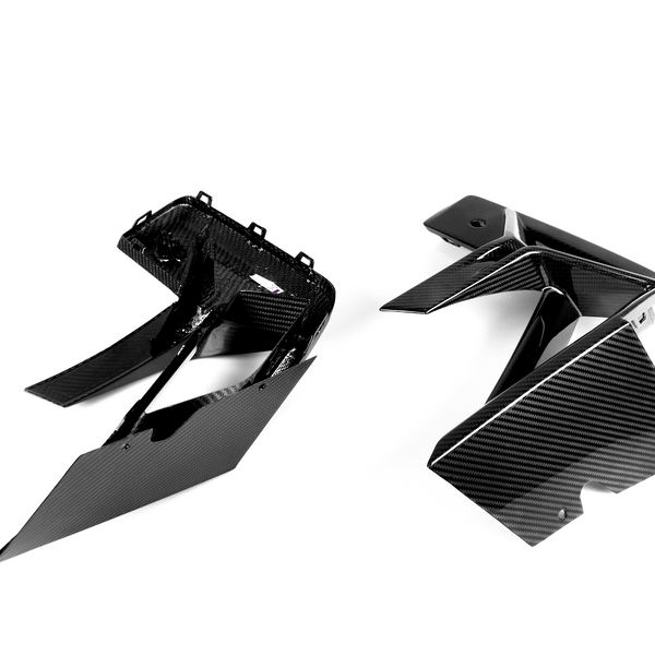 Two angular carbon fiber engine covers rest on a white surface. The glossy, woven texture suggests their lightweight, durable design commonly used in automotive applications.