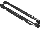 Two black carbon fiber side skirts are displayed, angled slightly apart, on a plain white background. The texture shows a diagonal weave pattern with small mounting holes along their length.