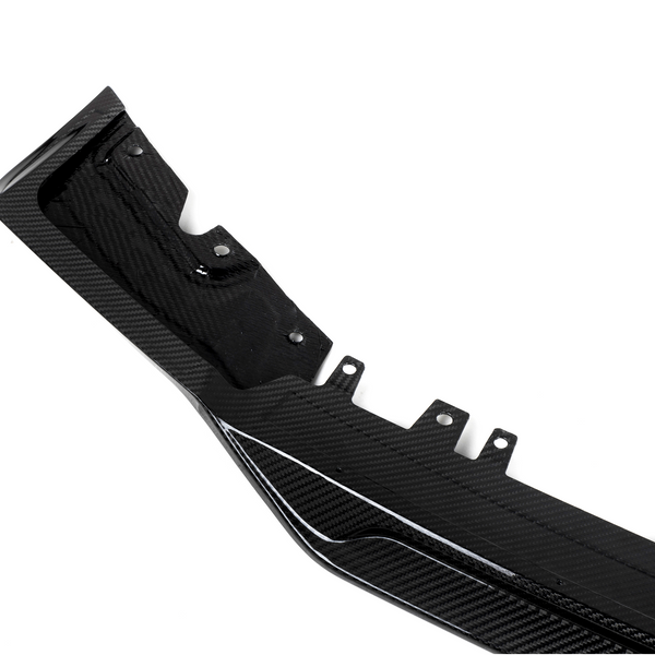 A black carbon fiber automotive component, featuring mounting points and textured patterns, lies against a plain white background.